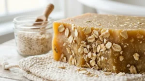 An extreme photorealistic close-up of the textured oatmeal and honey soap surface, revealing tiny embedded oat particles and a reference stone in natural light.