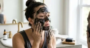 Woman applying rich black charcoal soap lather onto her face to cleanse acne-prone skin.